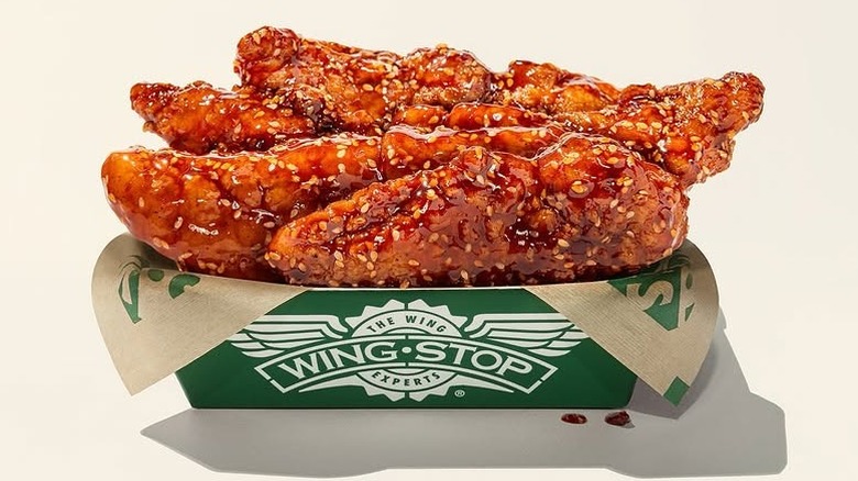 A close-up of a branded box of Wingstop wings covered in a sweet chili glaze, on a white background