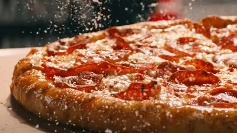 A screengrab of a cooked Domino's stuffed crust pepperoni pizza being sprinkled with powder