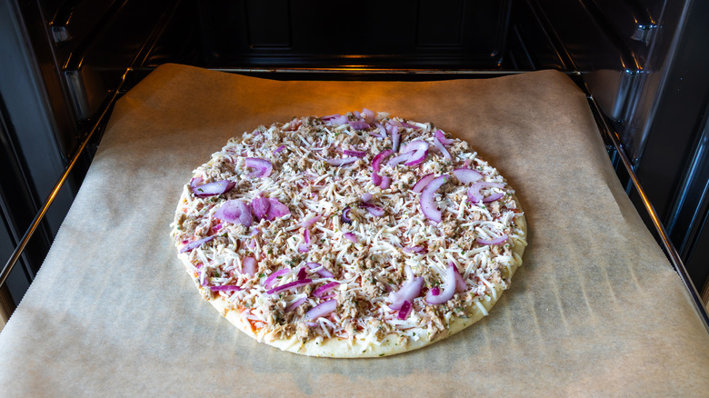 A frozen pizza sitting on a baking sheet about to go into an oven